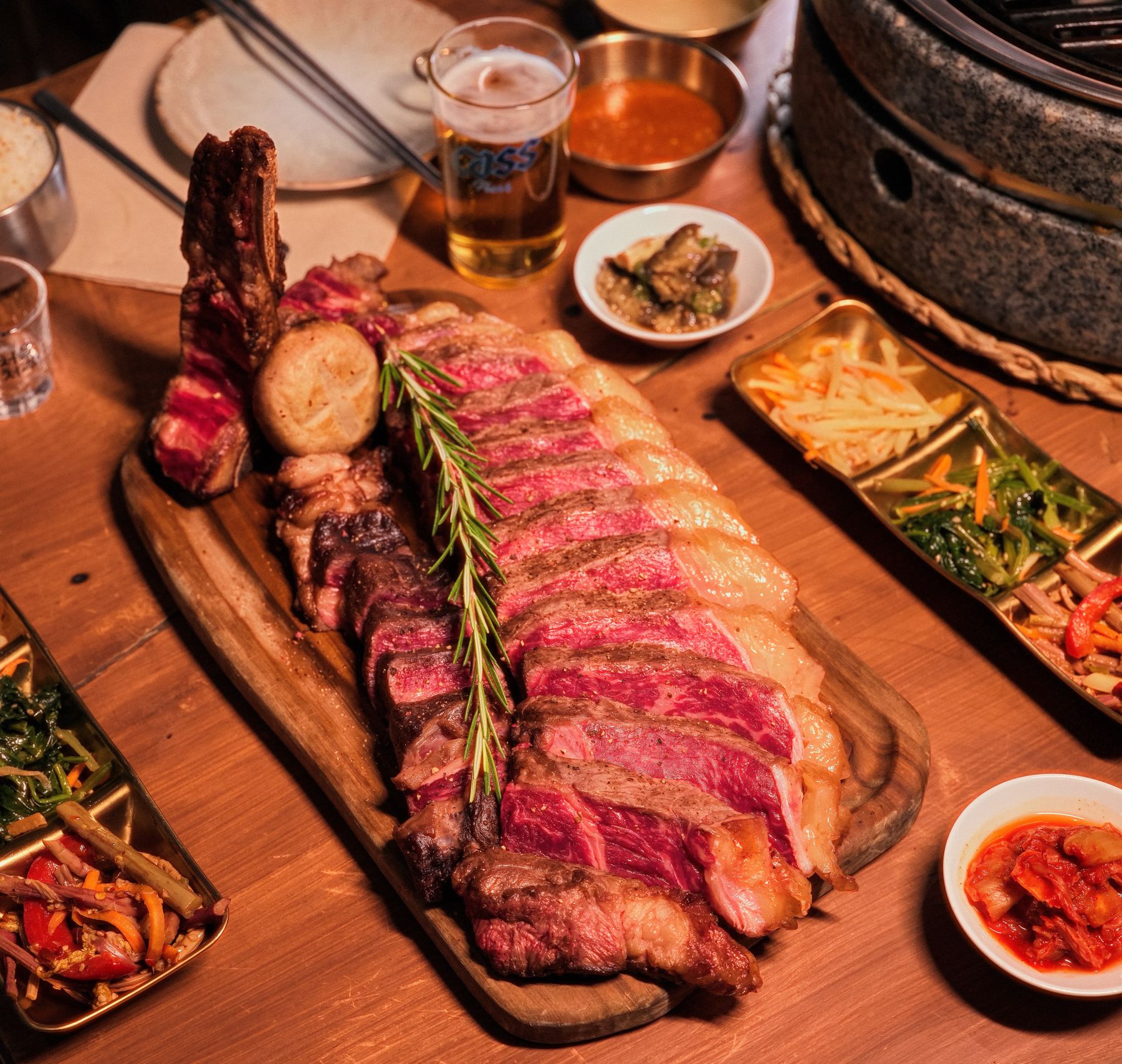 Costata tagliata a fette sul tagliere, con contorni e una birra Cass