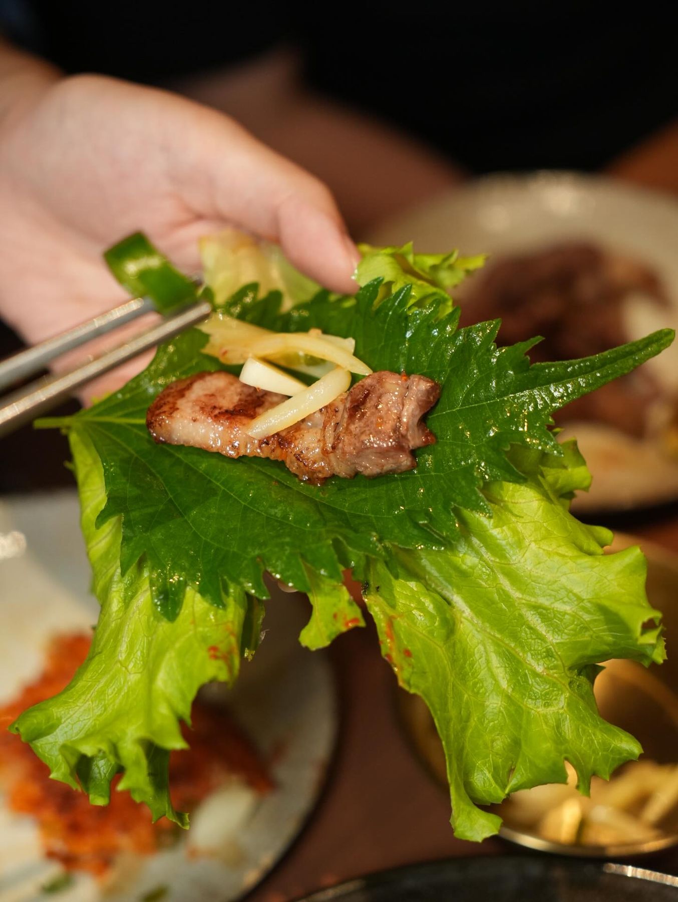 Un ssam: foglia di lattuga con carne e salsa tenuta in mano